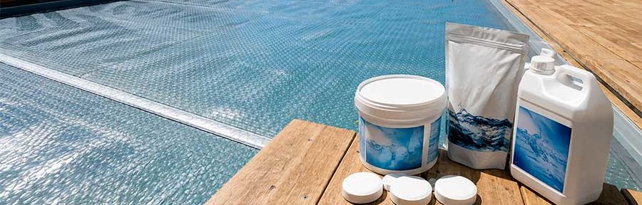 Bâche à bulles couvrant une piscine après traitement choc, avec produits chimiques pour piscine posés sur la terrasse en bois